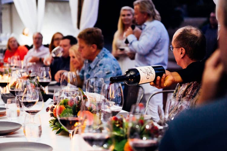 Weddings 38 A group of people sitting at a long table with wine glasses, enjoying a social gathering.