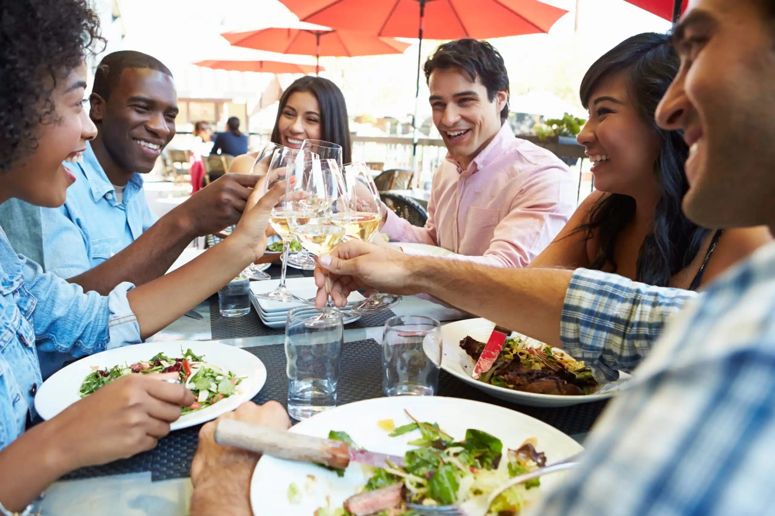 People dining and clinking glasses of white wine.