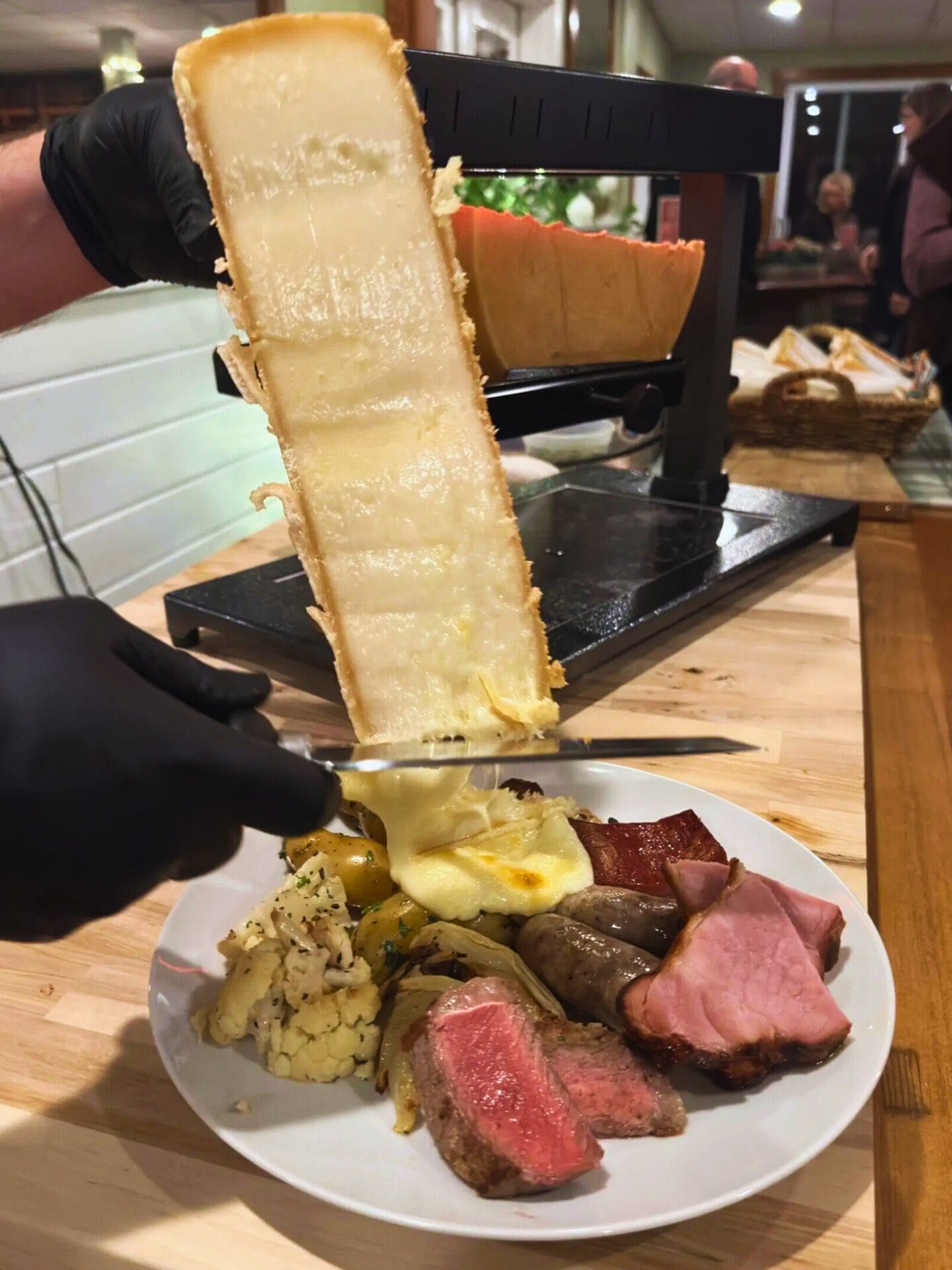 Scraping melted Raclette cheese over a dinner plate of meats and vegetables
