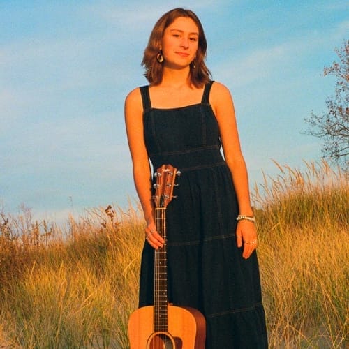 Zinnia with an acoustic guitar in a field of dune grass.