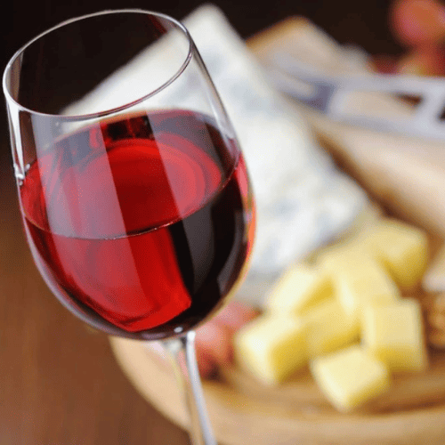 Glass of red wine with different cheeses in the background.