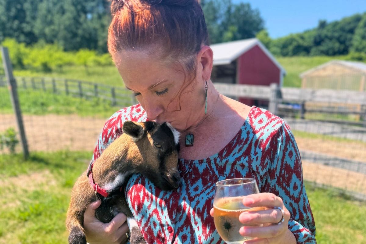 Women giving a goat a kiss on the head while holding a glass of wine