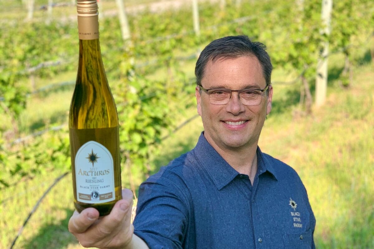 Winemaker, Lee Lutes, holding a bottle of Riesling in a vineyard.